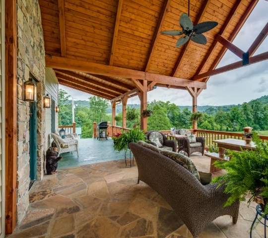 photo of covered porch outdoor living space with ceiling fan, stone floor and stone wall of home