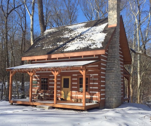 Photo of traditional chink log cabin with upper loft and covered front porch. Taken in the snow